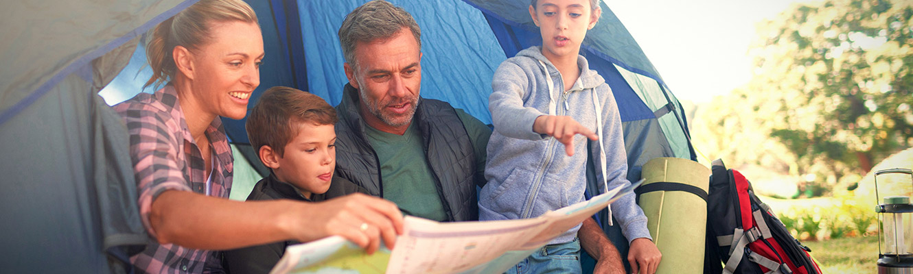 Family sitting outside their tent looking at a map while camping. 